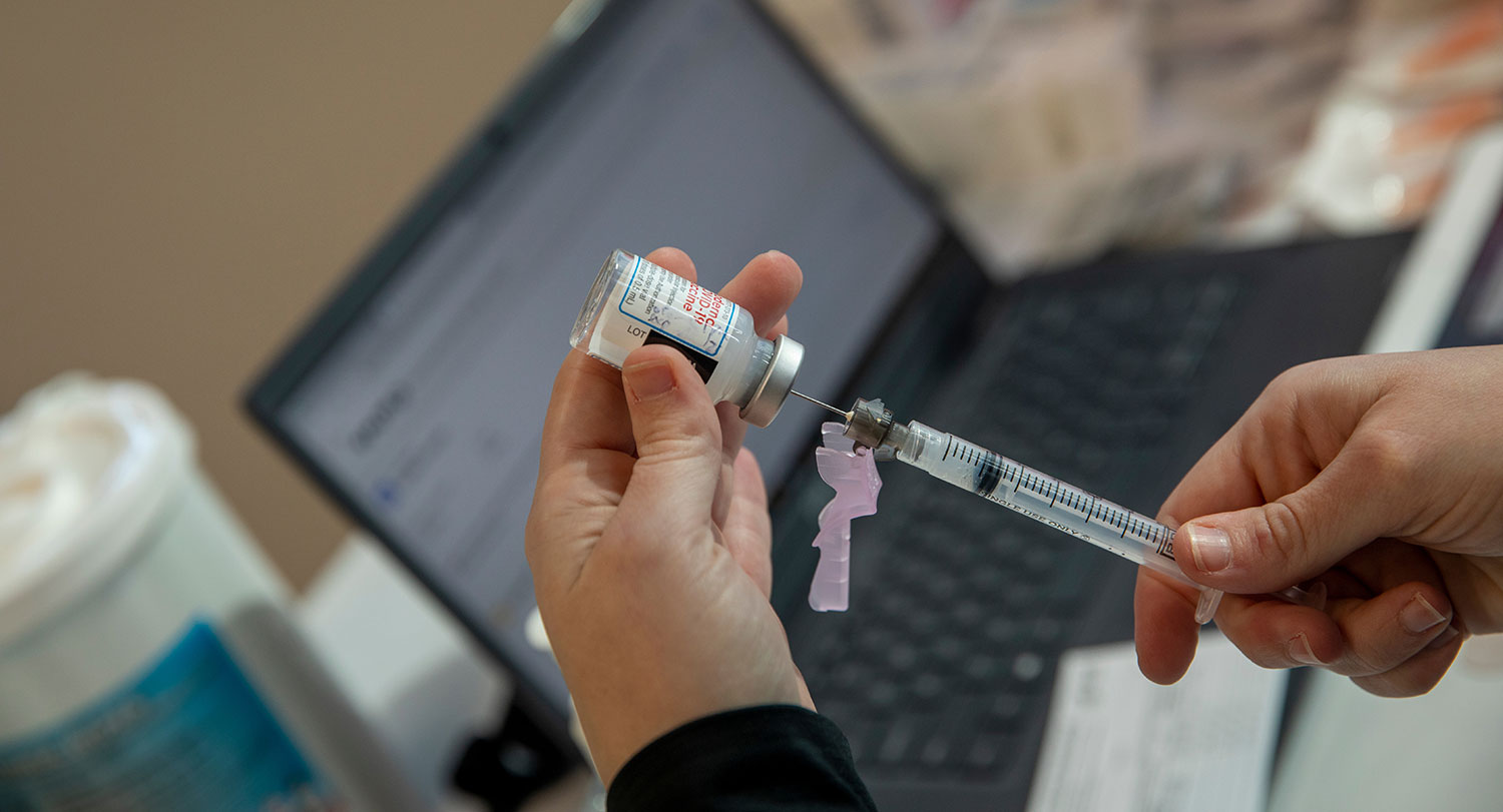 A closeup of a medical professional extracting a vaccine from a vial with a syringe