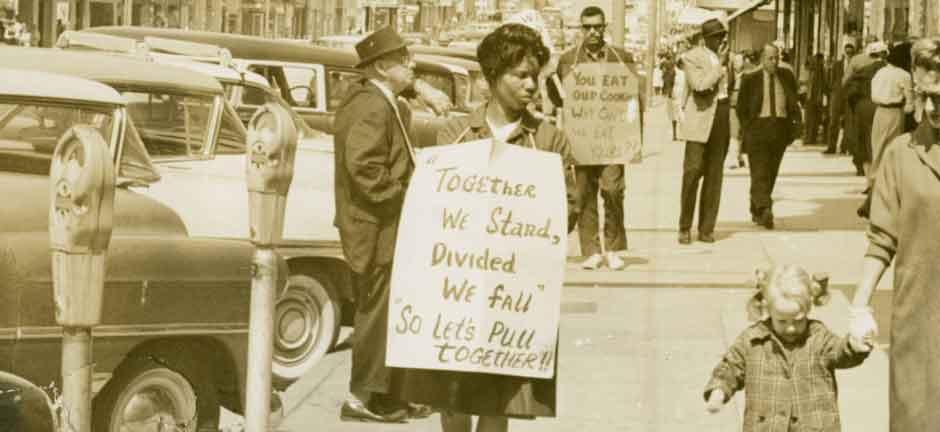 a Black woman holds a sign protesting segregation in the 1960s