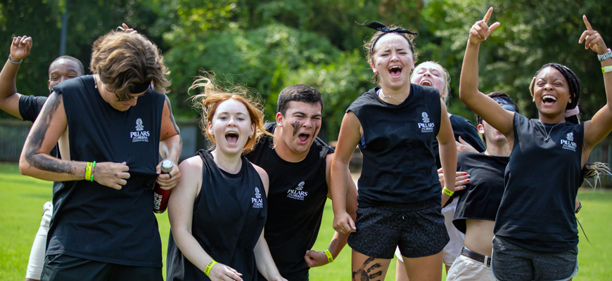 Students in black Pillars for Carolina T-shirts cheer during a field game