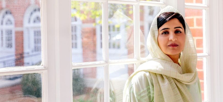 A woman stands in front of a window in traditional Pakistani dress