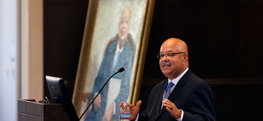 I.S. Leevy Johnson speaks at a lecture with his portrait in the background. 