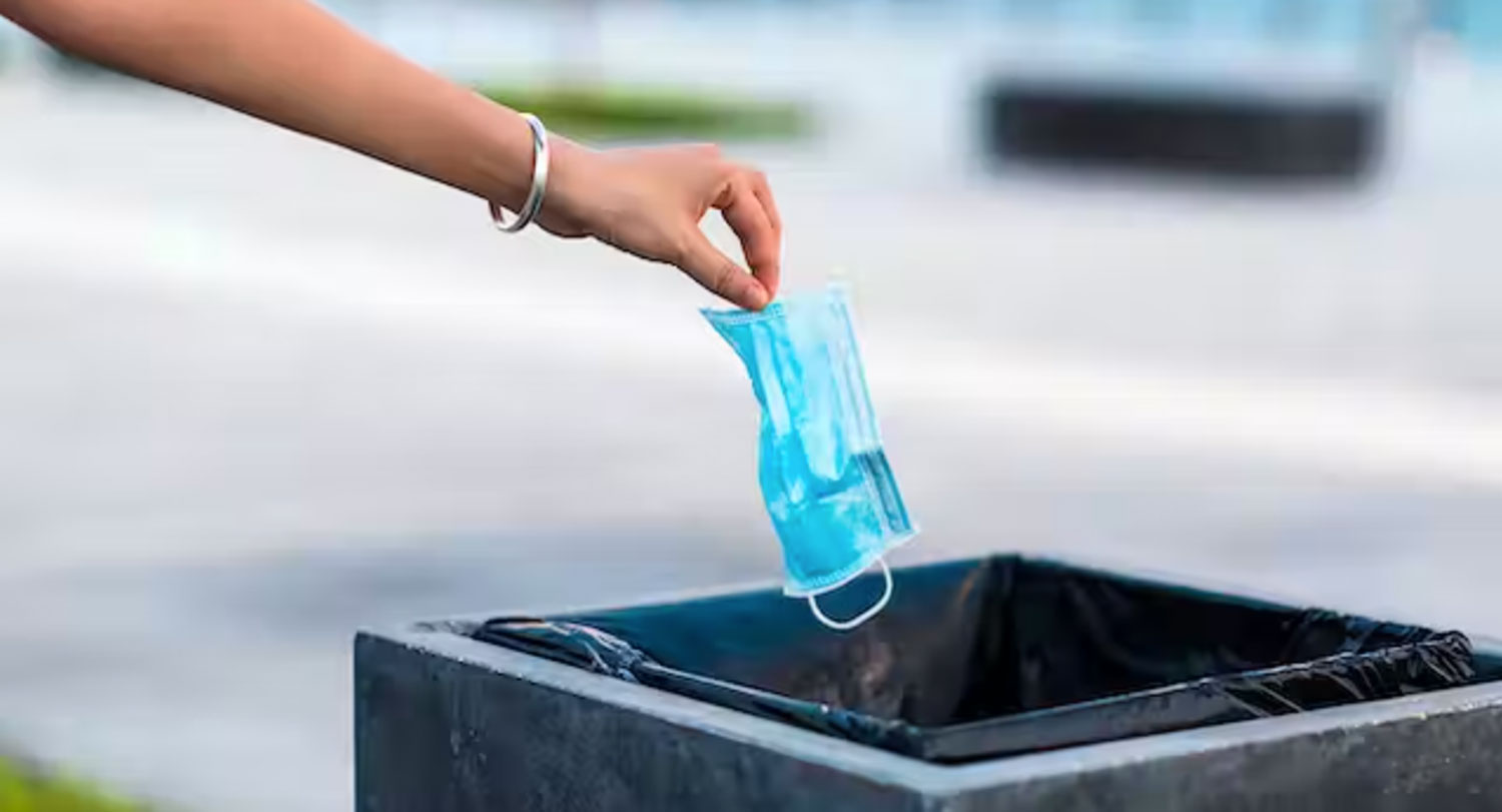 Hand drops surgical mask into a trash can