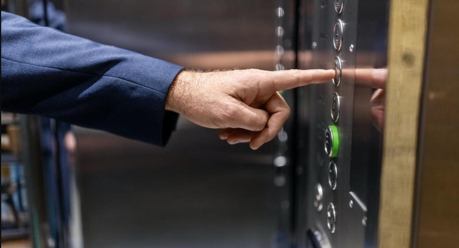 A hand presses an elevator button