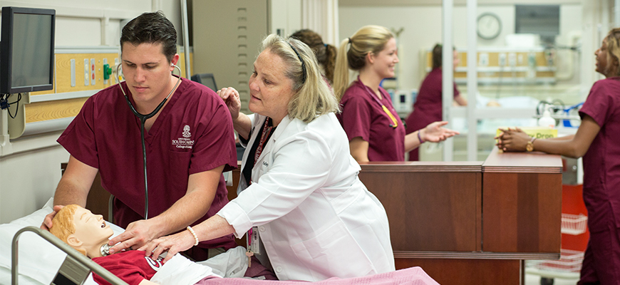 A nursing student practices on a mannekin while a professor observes. 