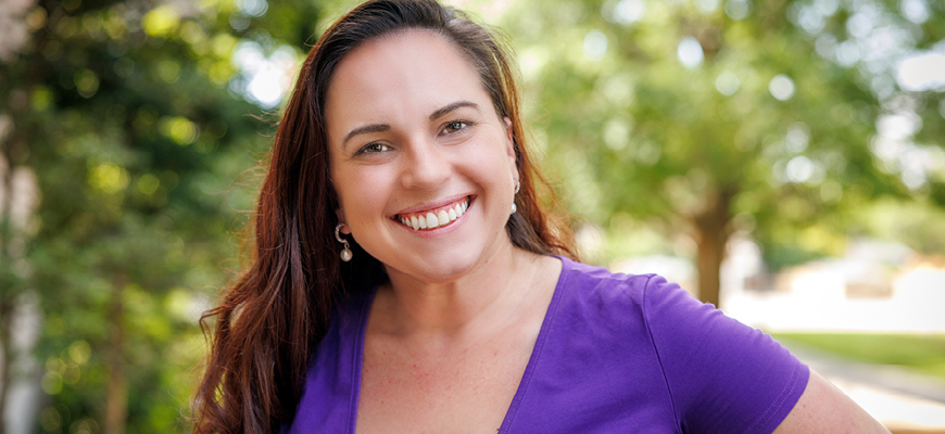 alumna Taylor Wilson poses at the State House wearing a purple shirt