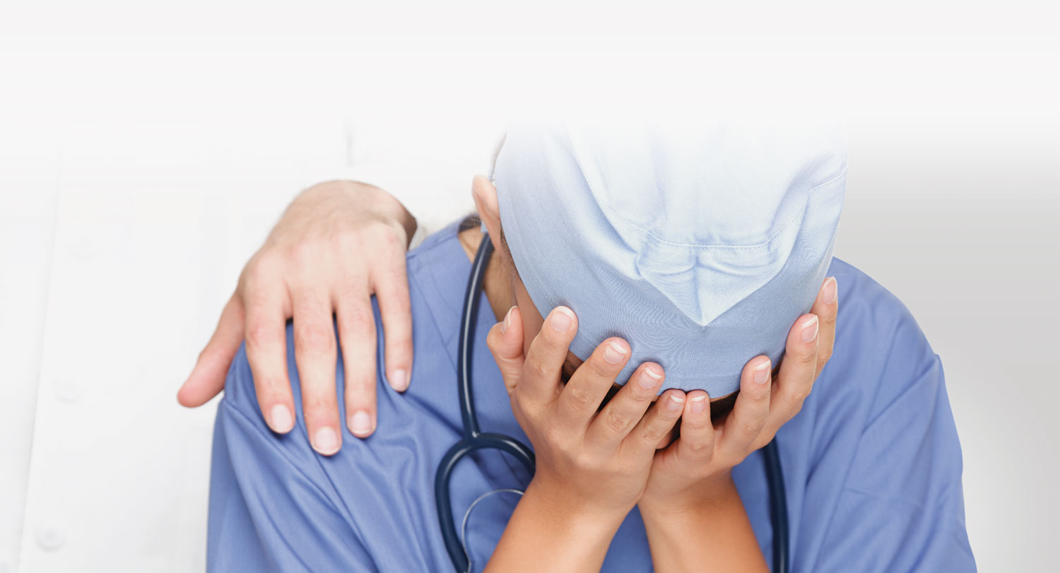 A healthcare worker wearing scrubs with his/her hands over face indicating frustration.