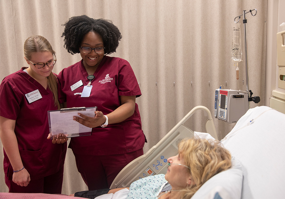 Two USC student nurses stand at the bedside of a patient