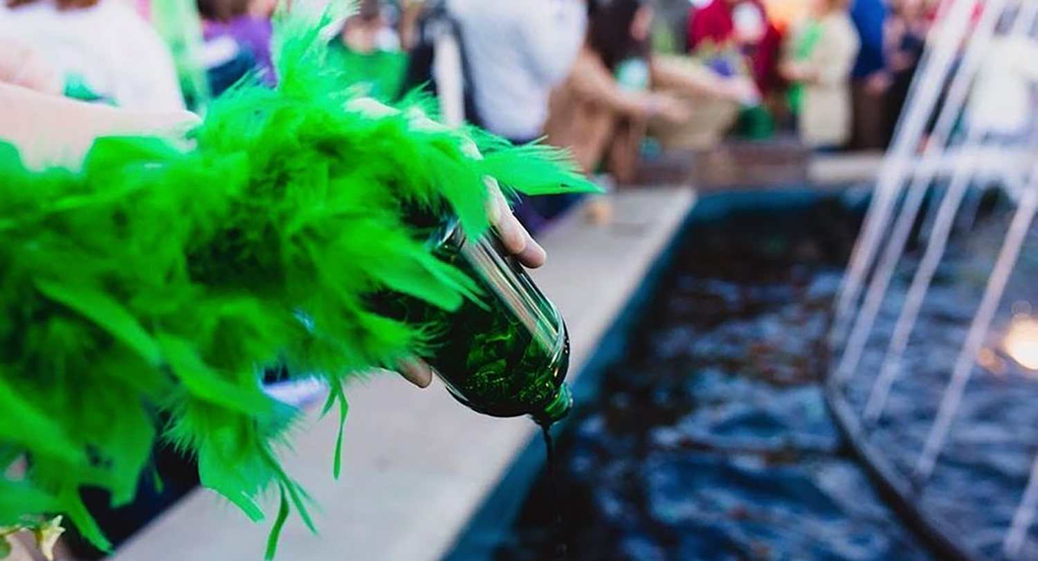 a hand pouring a bottle of green dye in a fountain