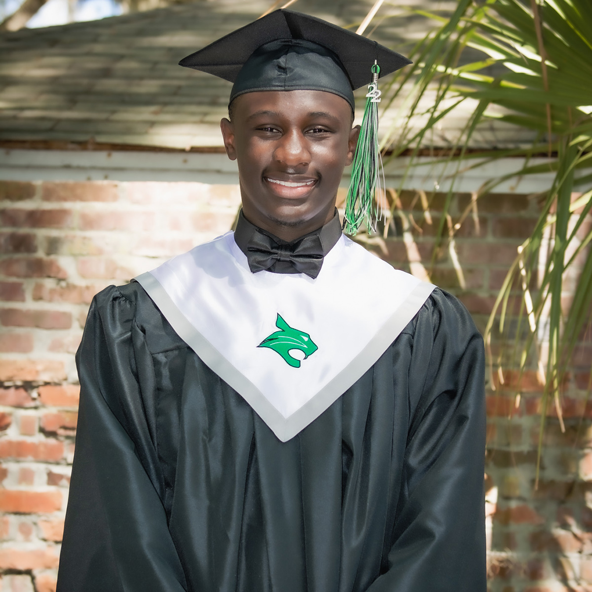 Man in cap and gown standing in front of brick wall