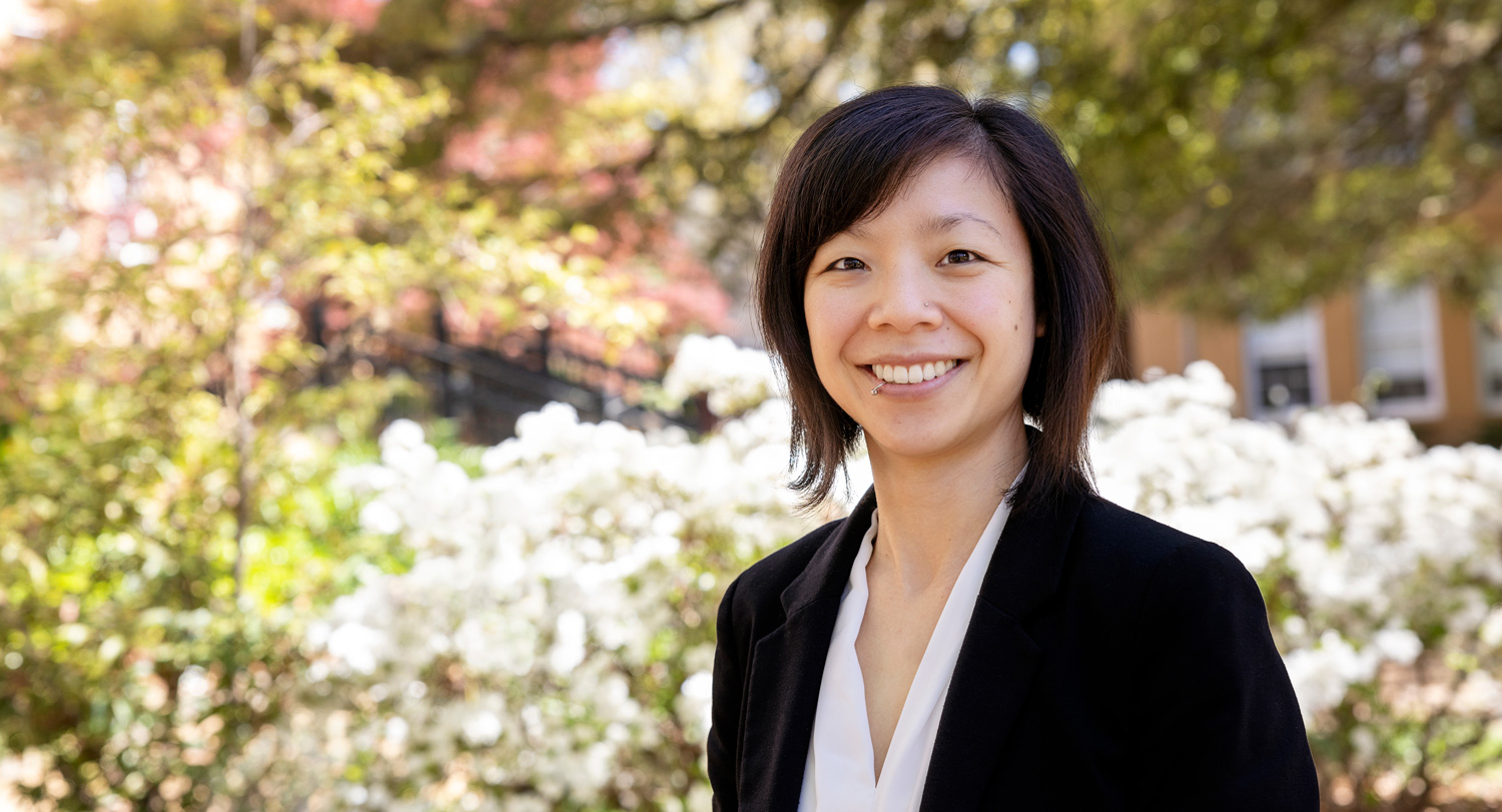 Jaclyn Wong wears a white shirt and a black blazer in front of white flowers