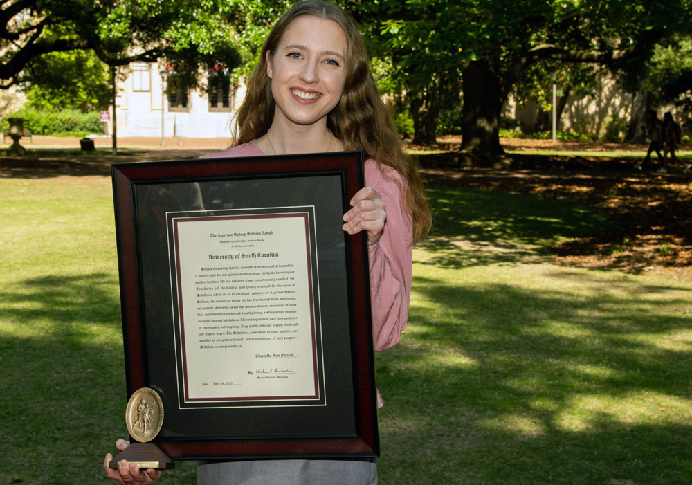 Charlotte pollack stands on the horseshoe holding a large framed award