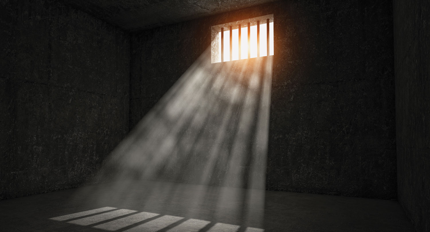 A photo of an empty prison cell with light shining through a window.