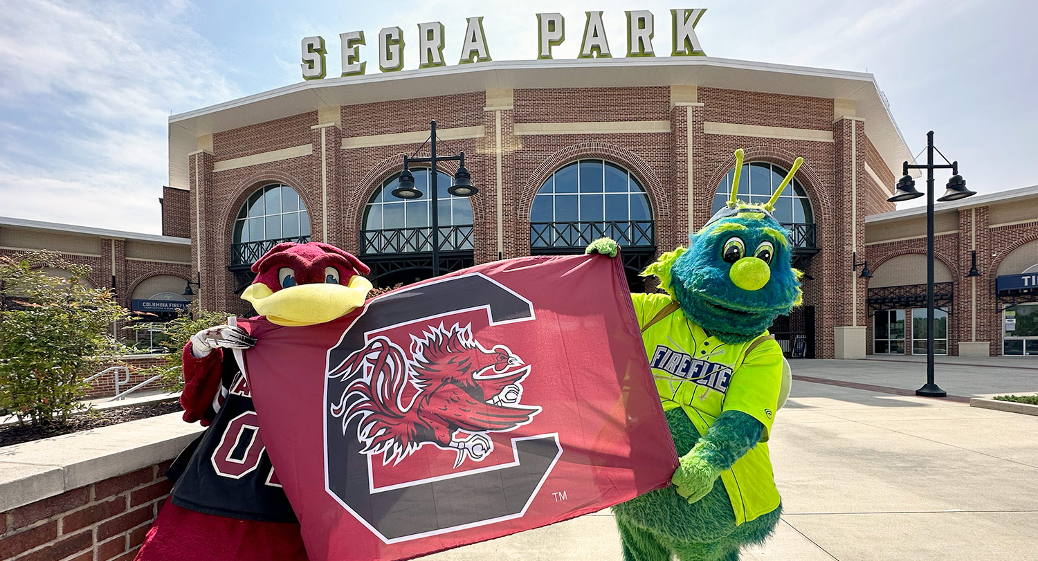 Cocky and Mason holding a Gamecock flag in front of Segra park