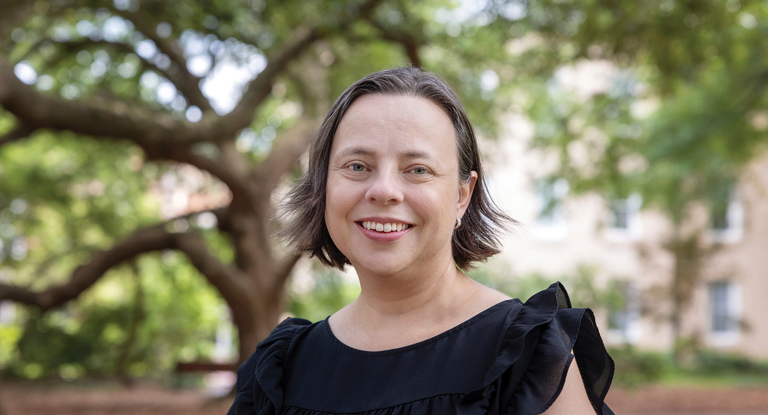 April Hiscox smiles in front of a tree.
