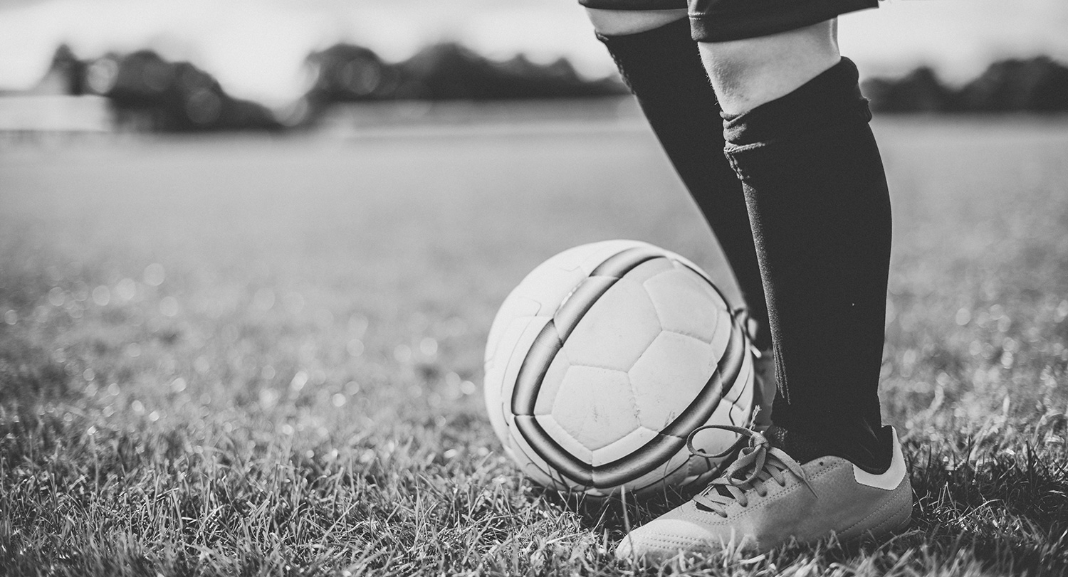 A kid with soccer gear on with a soccer ball at their feet.