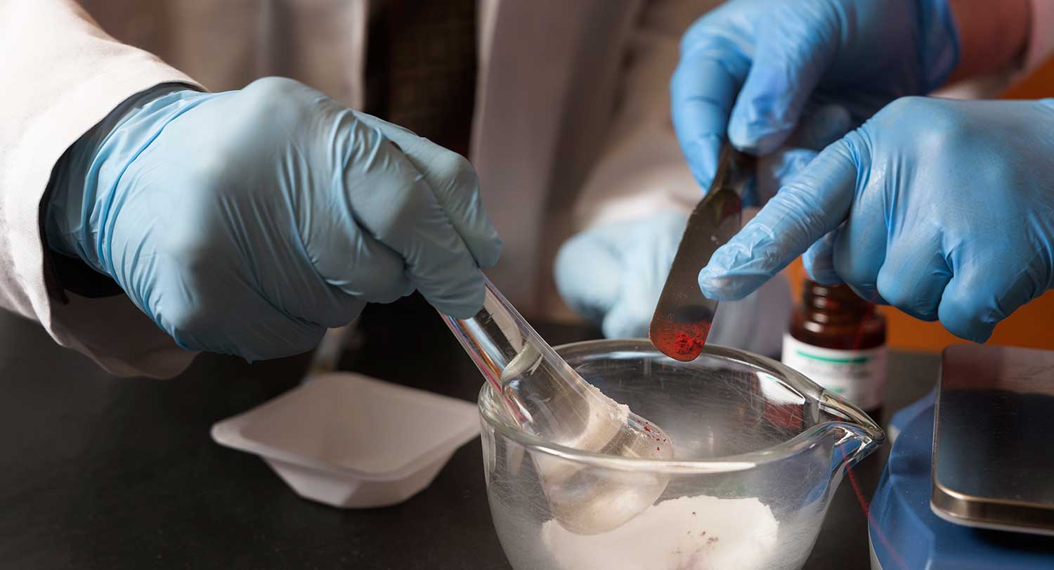 Two sets of hands mix chemicals in a pharmacy