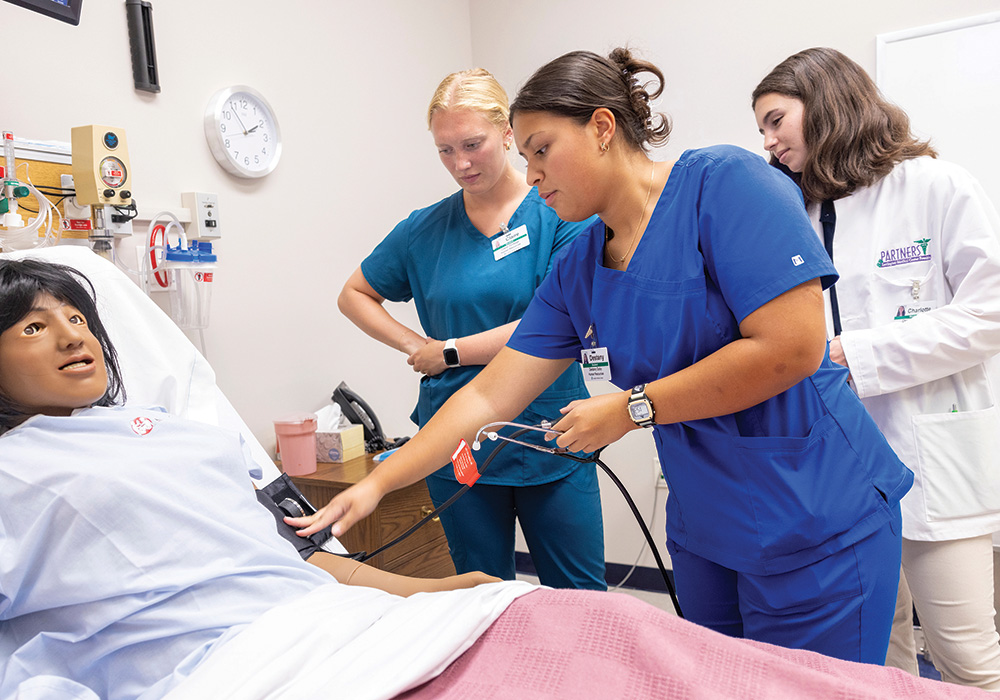 An instructor oversees two nursing students at a human health simulator.