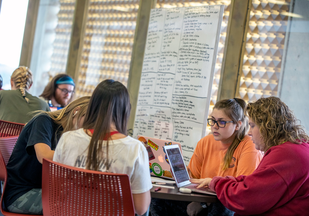 Students sit at a table, using their laptops to study.