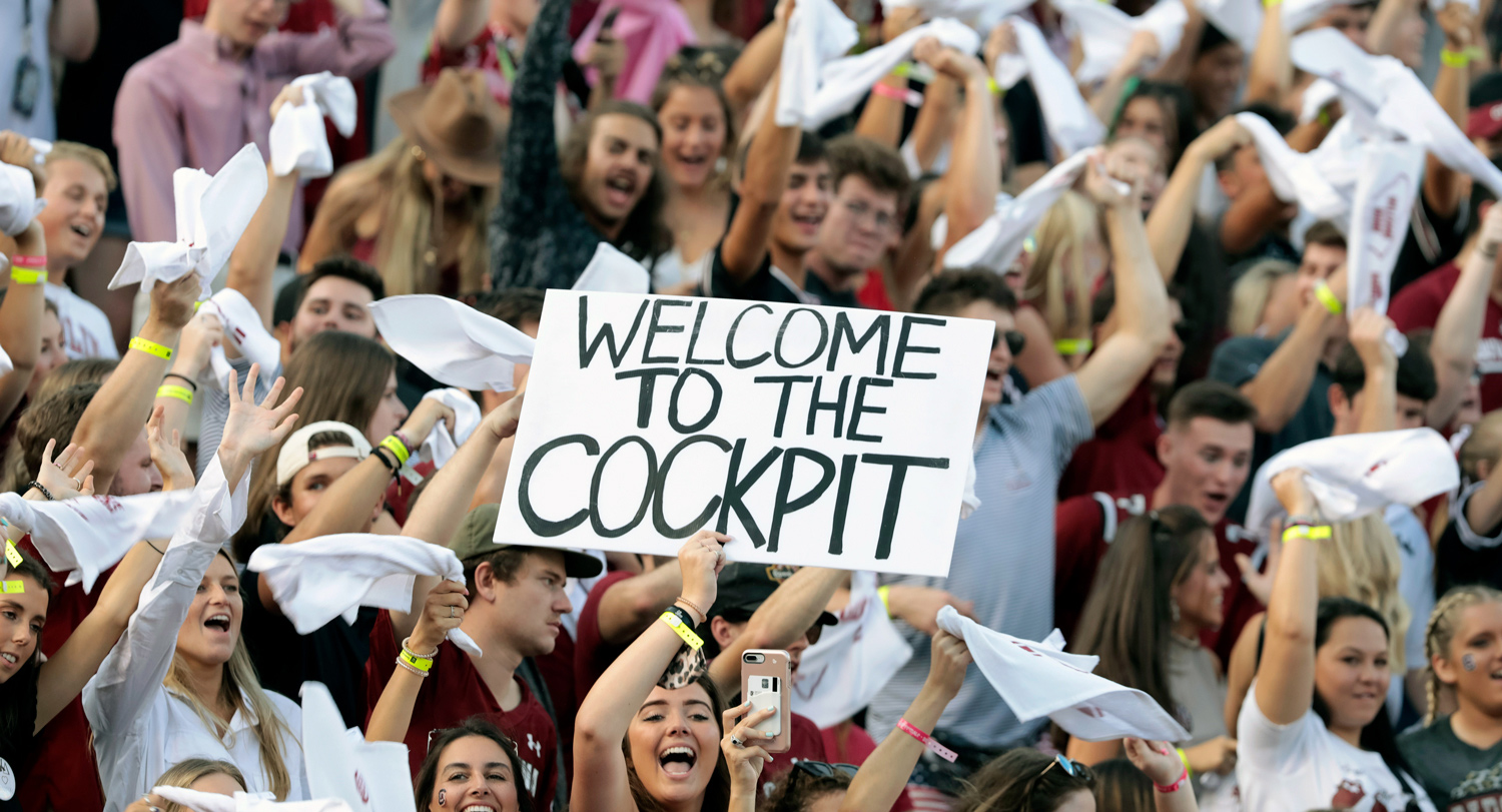 Woman holds "Welcome to the Cockpit" sign at a football game.