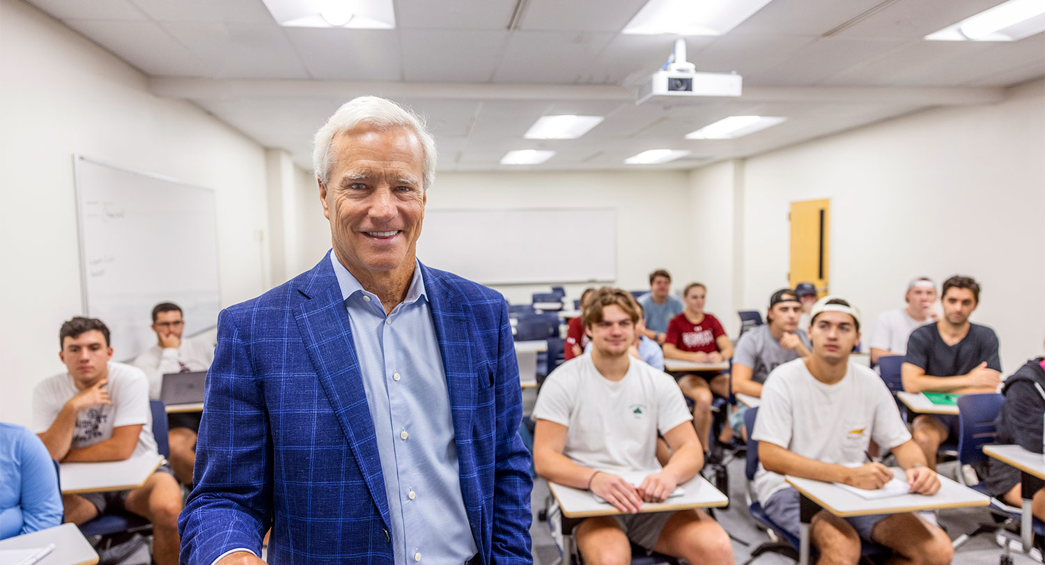 Danny Morrison stands in front of classroom with students behind him