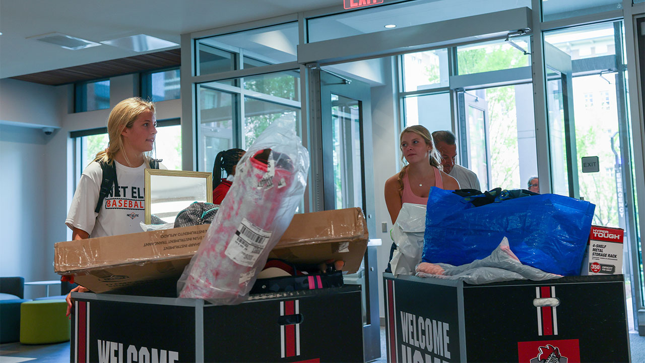 Two freshmen pushing carts with their belongings into their new campus home.