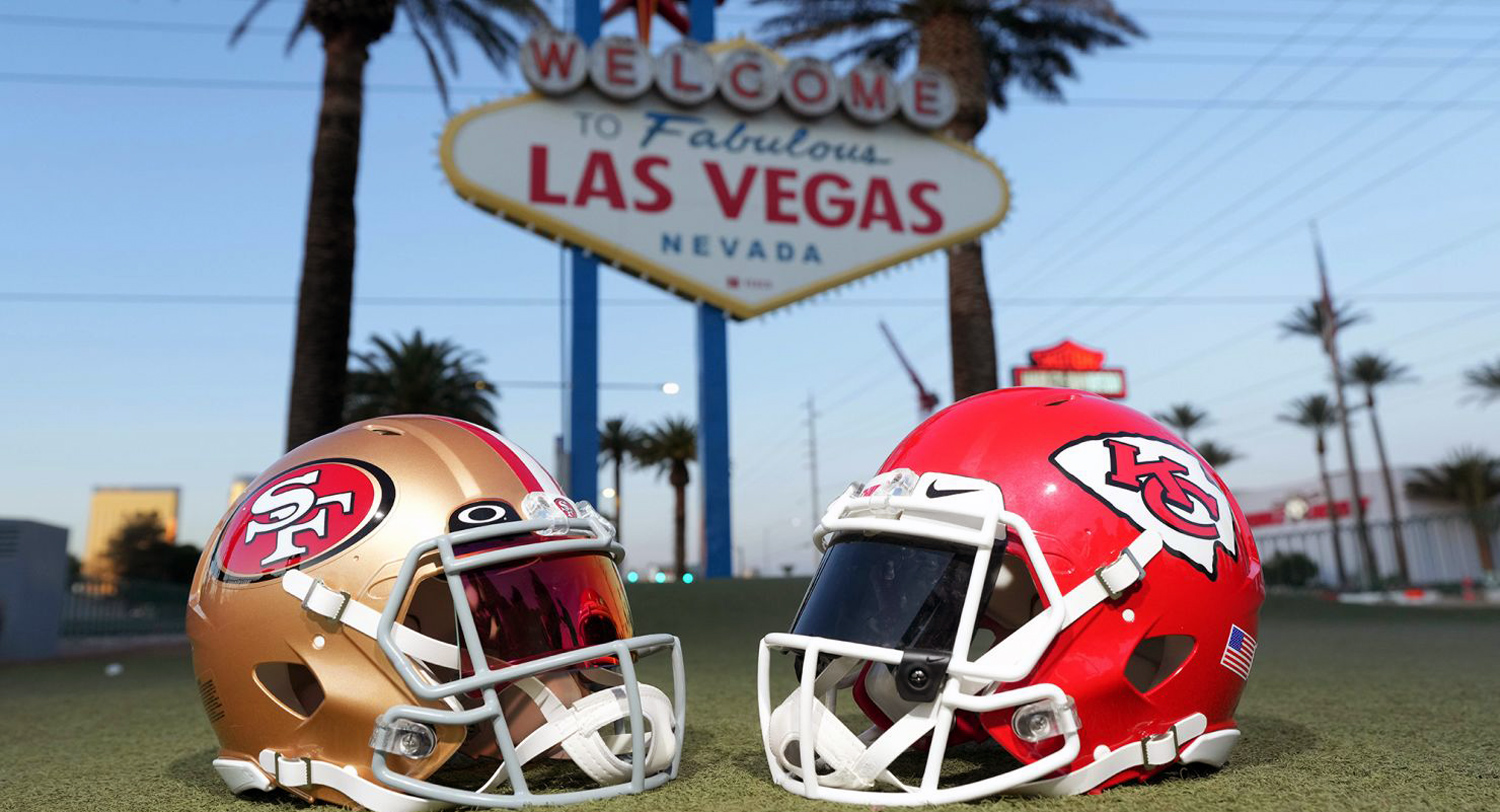 A gold helmet and a red helmet sit on the ground with a sign behind them that reads, "Welcome to Fabulous Las Vegas Nevada."