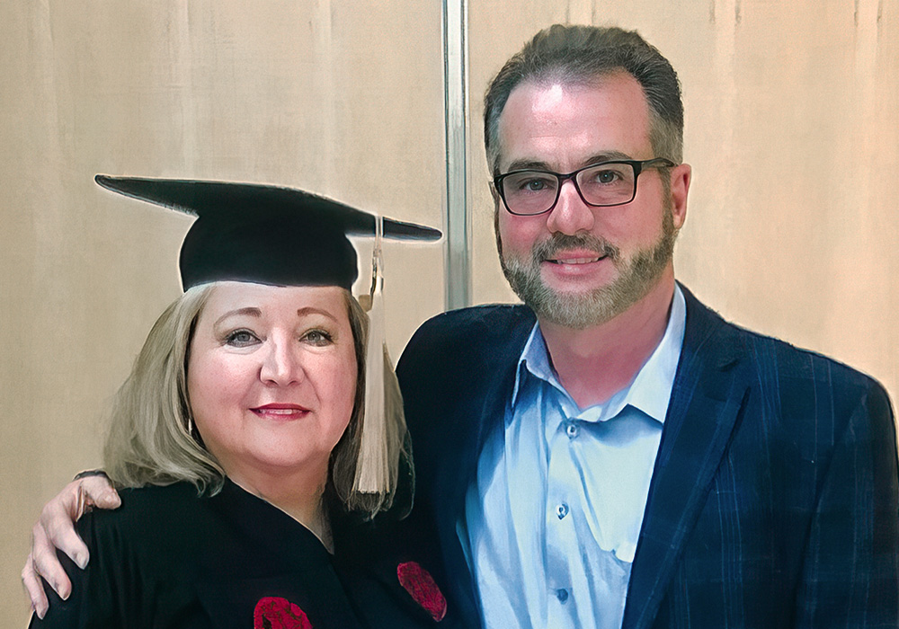 Sandra Edwards, posing with her husband, in a cap and gown, celebrates graduating with a master's degree from the Darla Moore School of Business.