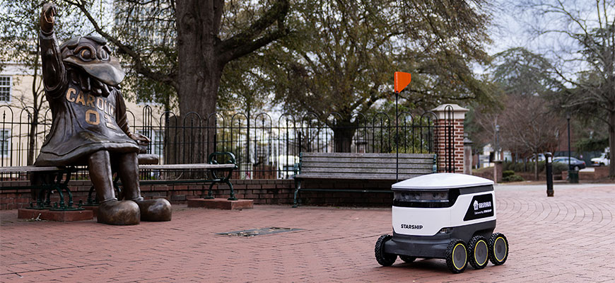 A Starship food delivery robot rolling past the Cocky statue near Greene Street