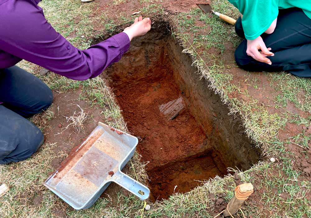 Two people uncover a piece of wood inside a hole at an excavation site