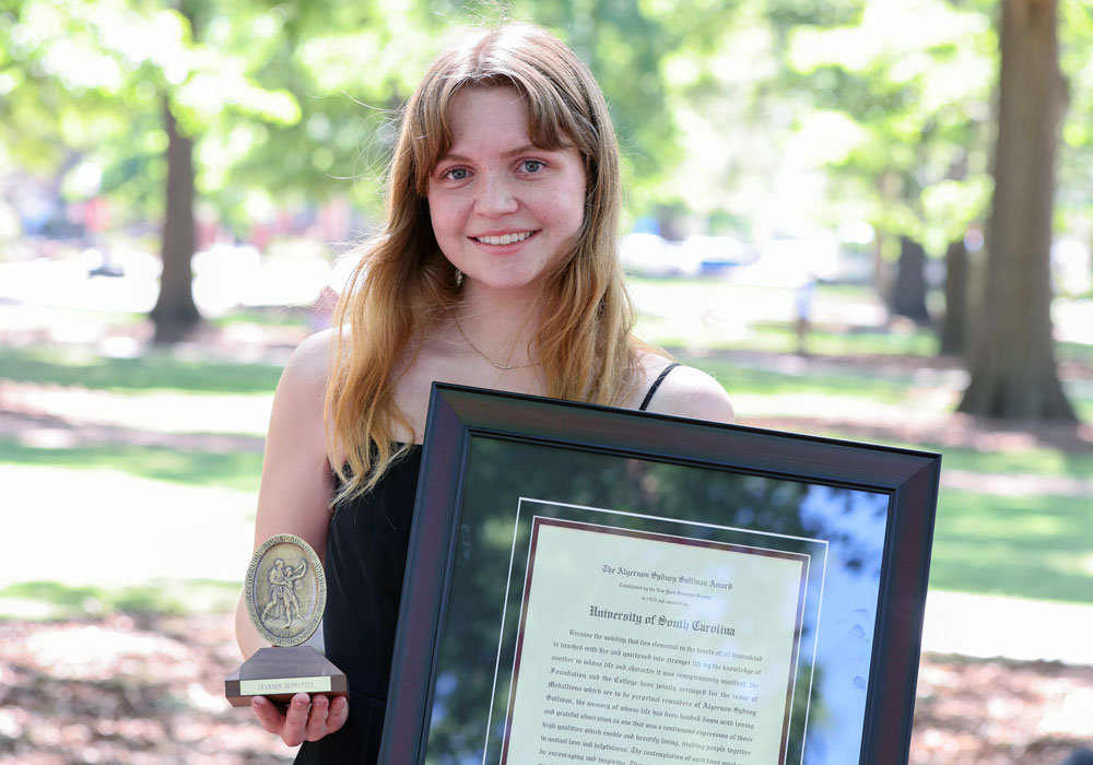 woman holds a framed award with trees in the background