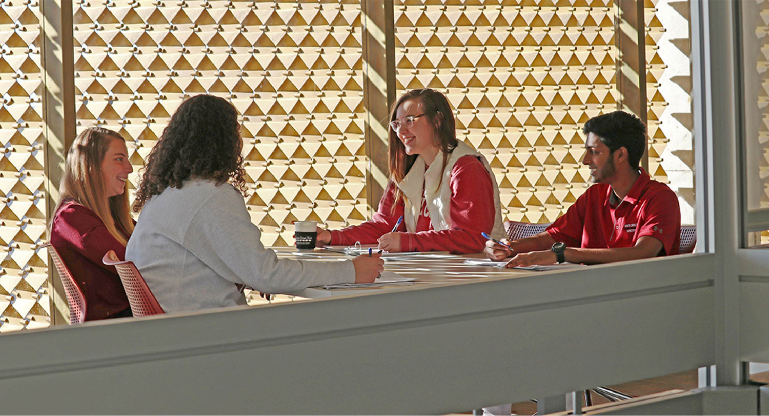 Four students engaged in conversation and work sit at a table in Thomas Cooper Library