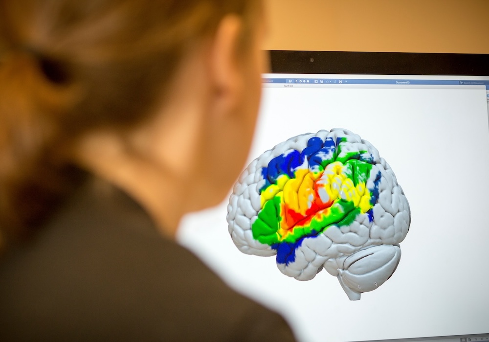 Multicolored brain scan on computer screen over shoulder of researcher