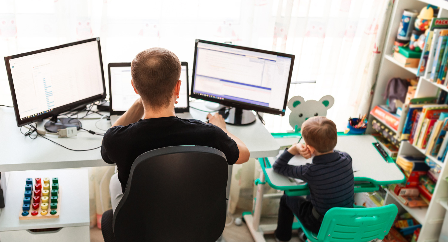 Man sits at desk with child at smaller desk next to him