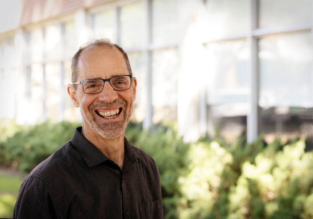 Carbone smiles broadly outside a campus building on a sunny day