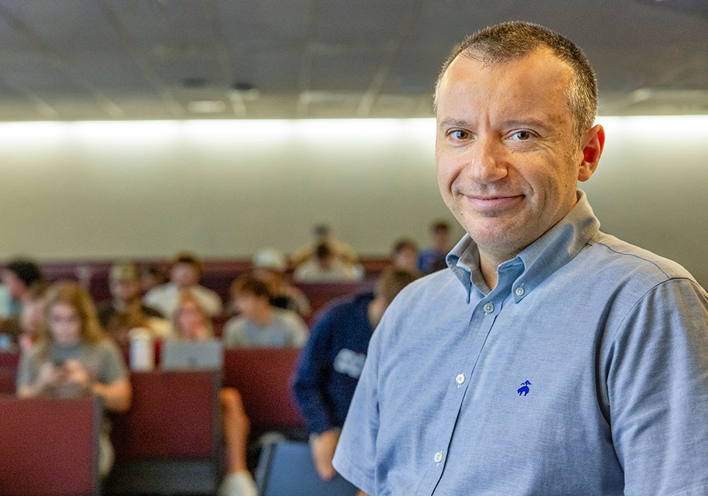 Nikos smiles in the classroom as students take their seats behind him.