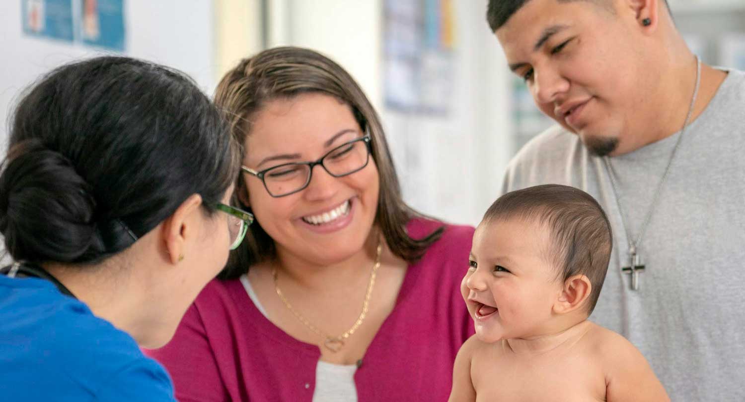 A health care provider greets a mother, father and their infant.