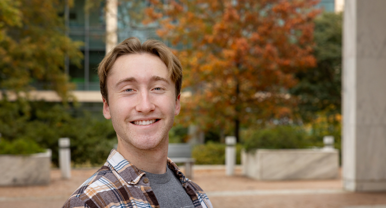 man stands outside with trees and a building in the background