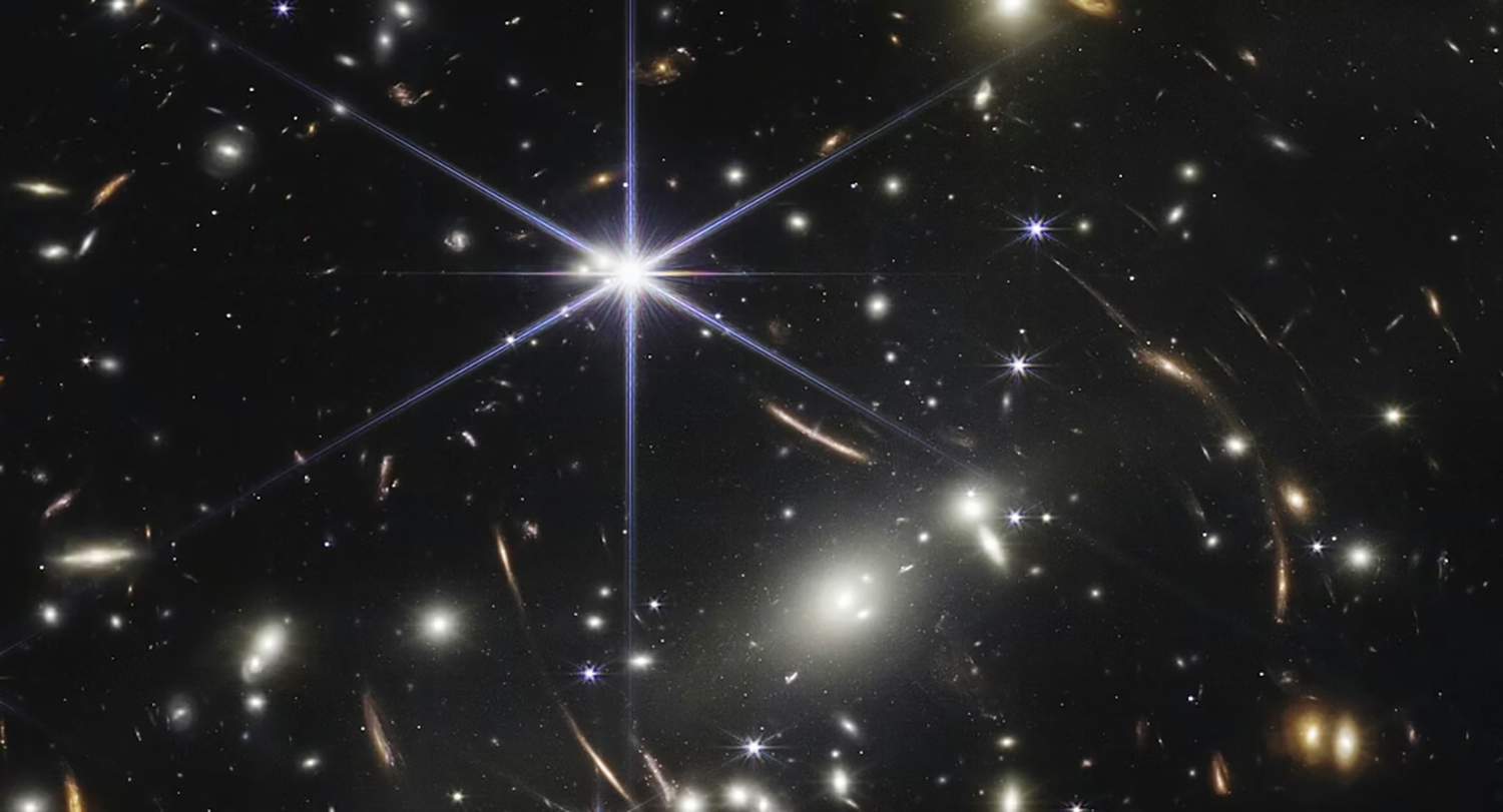 An image from NASA’s James Webb Space Telescope shows the dense galaxy cluster SMACS 0723, filled with thousands of galaxies—from bright ellipticals to faint red spirals—with gravitational lensing stretching distant background galaxies into curved streaks of light.