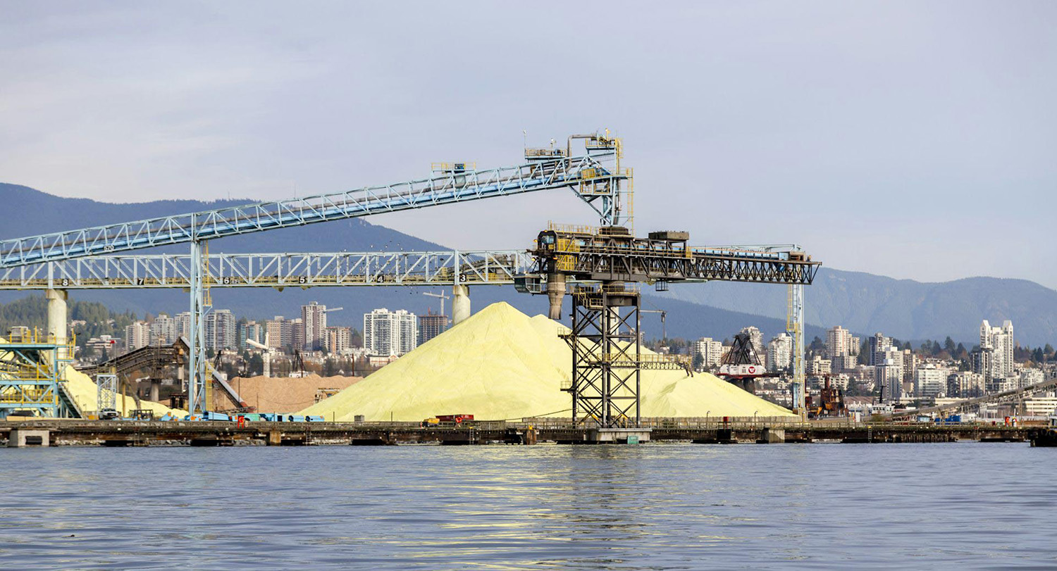 A pile of sulfur sits near a crane at a seaport.