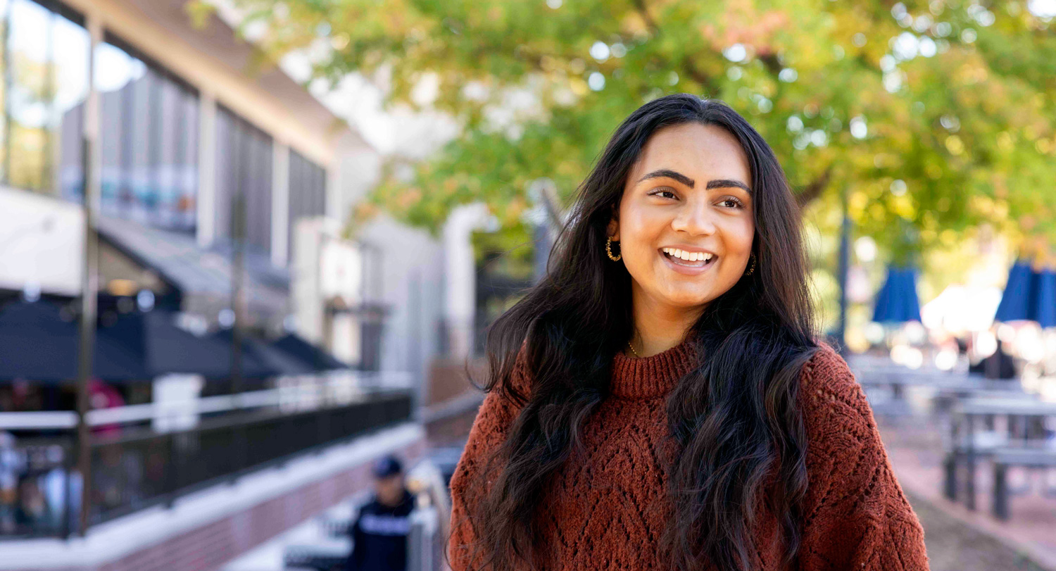 Head and shoulders image of a woman standing outside with building and trees in the background.