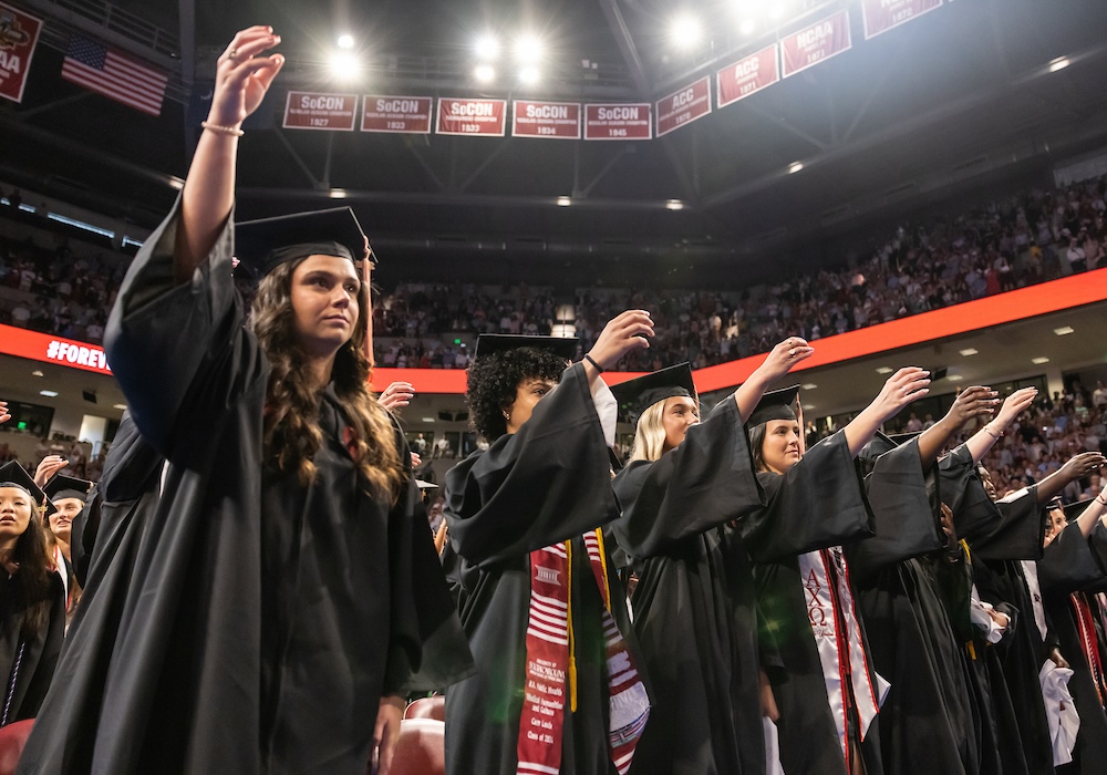 group of students holding arms up as a toast while wearing graduation robes