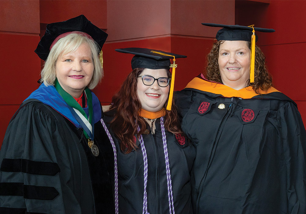 Three woman stand in cap and gowns at College of Nursing commencement