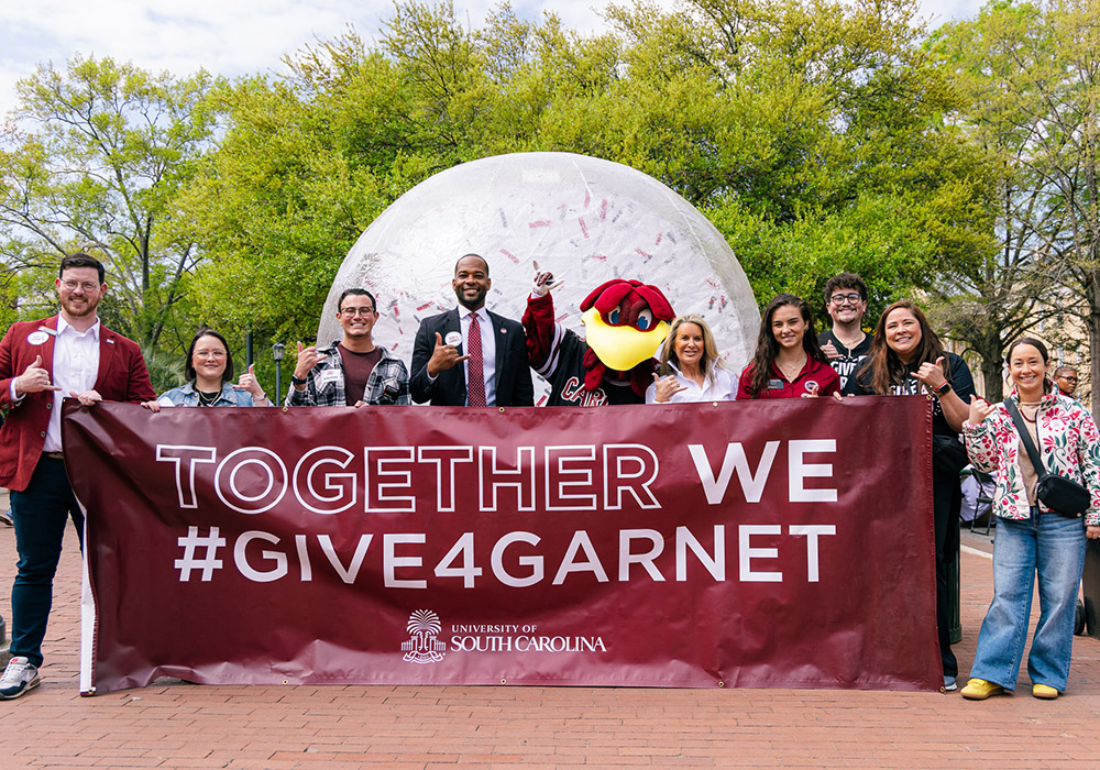 A group photo of university supporters holding a Give 4 Garnet banner at the Greene Street giving event.