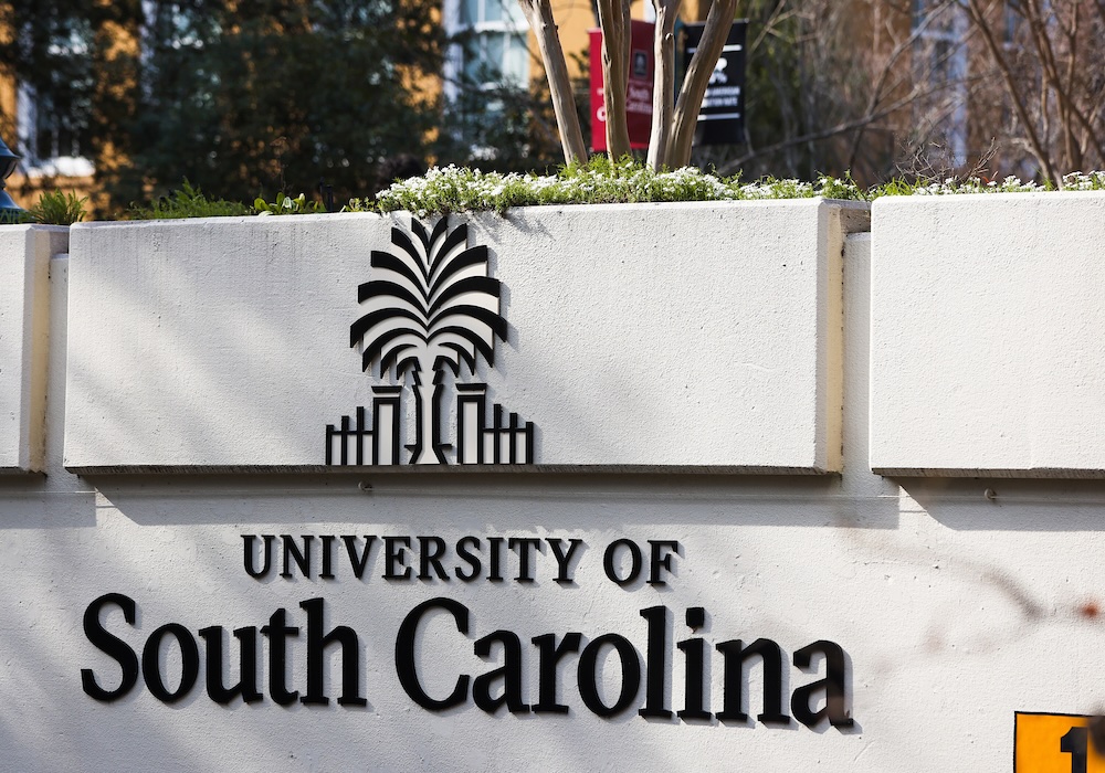 Entrance sign reading University of South Carolina with palmetto tree logo set against landscaped campus background