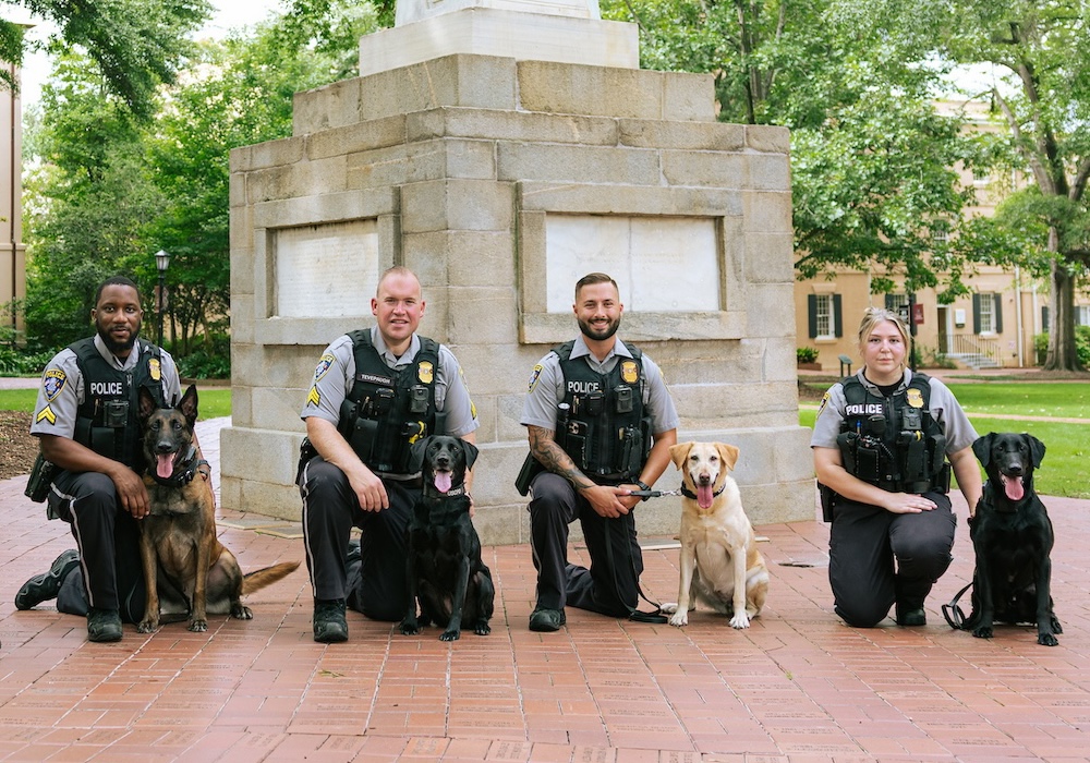 group of four police officers kneeling with their K-9 dogs in front of the Maxcy monument