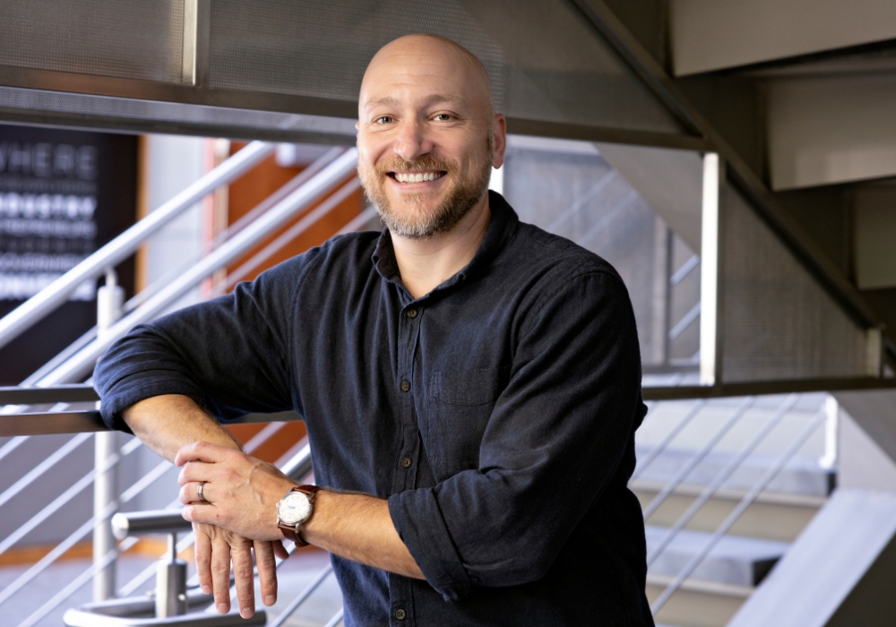 Aaron Vannucci stands by a staircase and smiles.