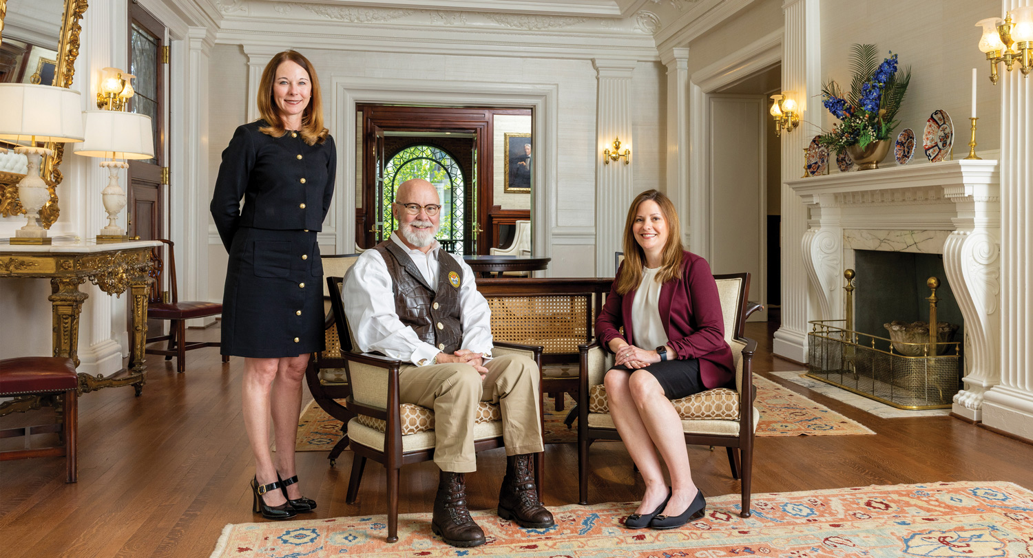 University of South Carolina School of Law alumni Emily Farr, Thomas Mullikin and Dolly Garfield pose in a formal historic room with a fireplace.