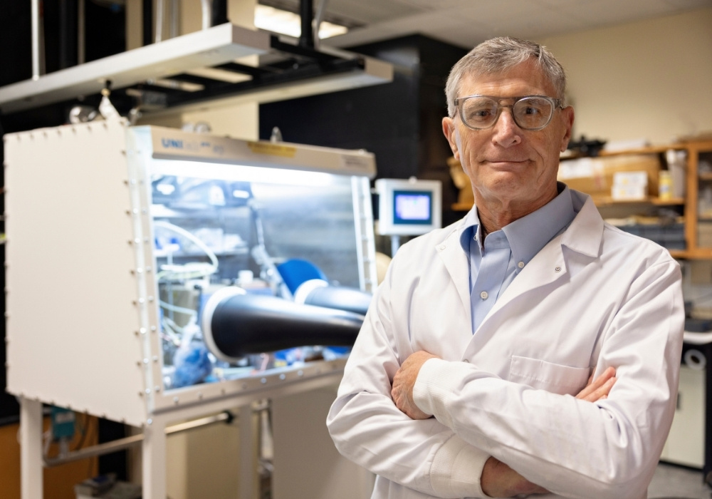 Ted Besmann poses for a photo in his lab. He's wearing glasses and a lab coat.