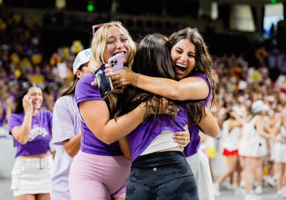 In front of a large crowd, three women hug excitedly during Bid Day at USC in 2025