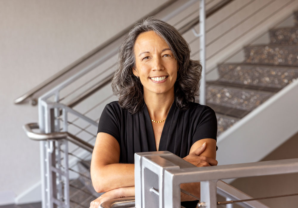 Stephanie Schaller smiles and crosses her arms in front of a staircase